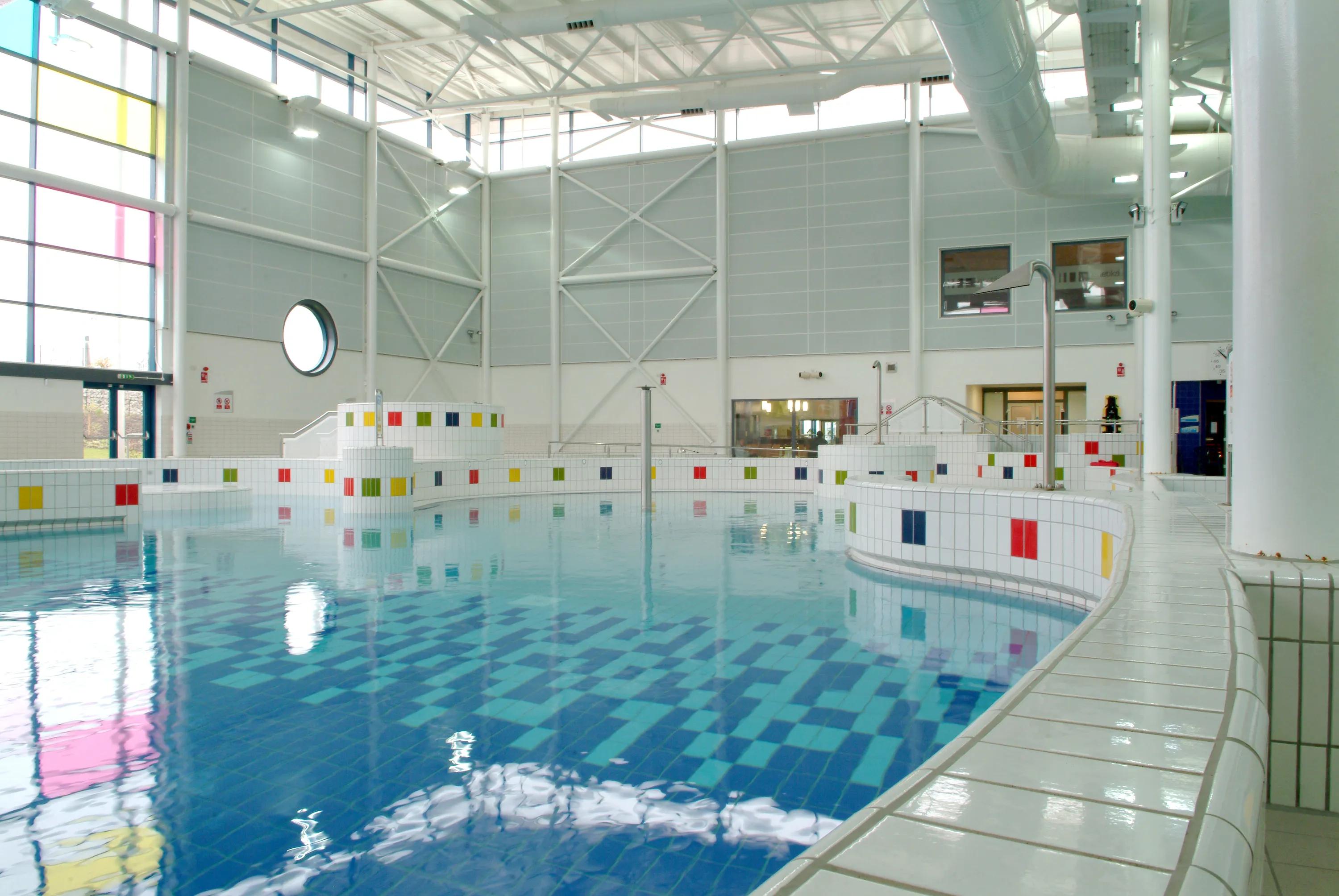 Indoor leisure pool with Rockfon Color-all wall absorbers, tiled pool edges with coloured accents, and a bright, open hall with large windows and high ceilings.