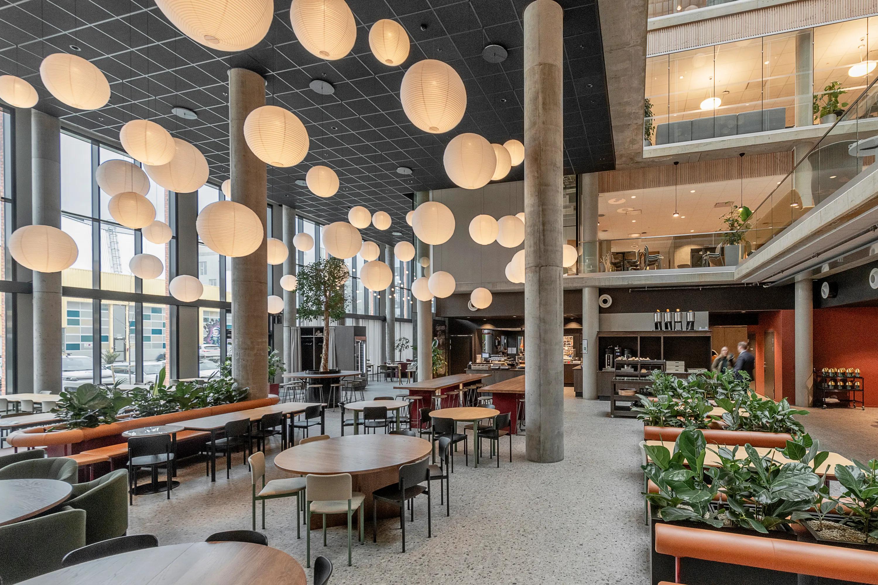 Office atrium with black suspended ceiling, seating areas, pendant globe lighting, and a black acoustic grid ceiling installed beneath a mezzanine level.