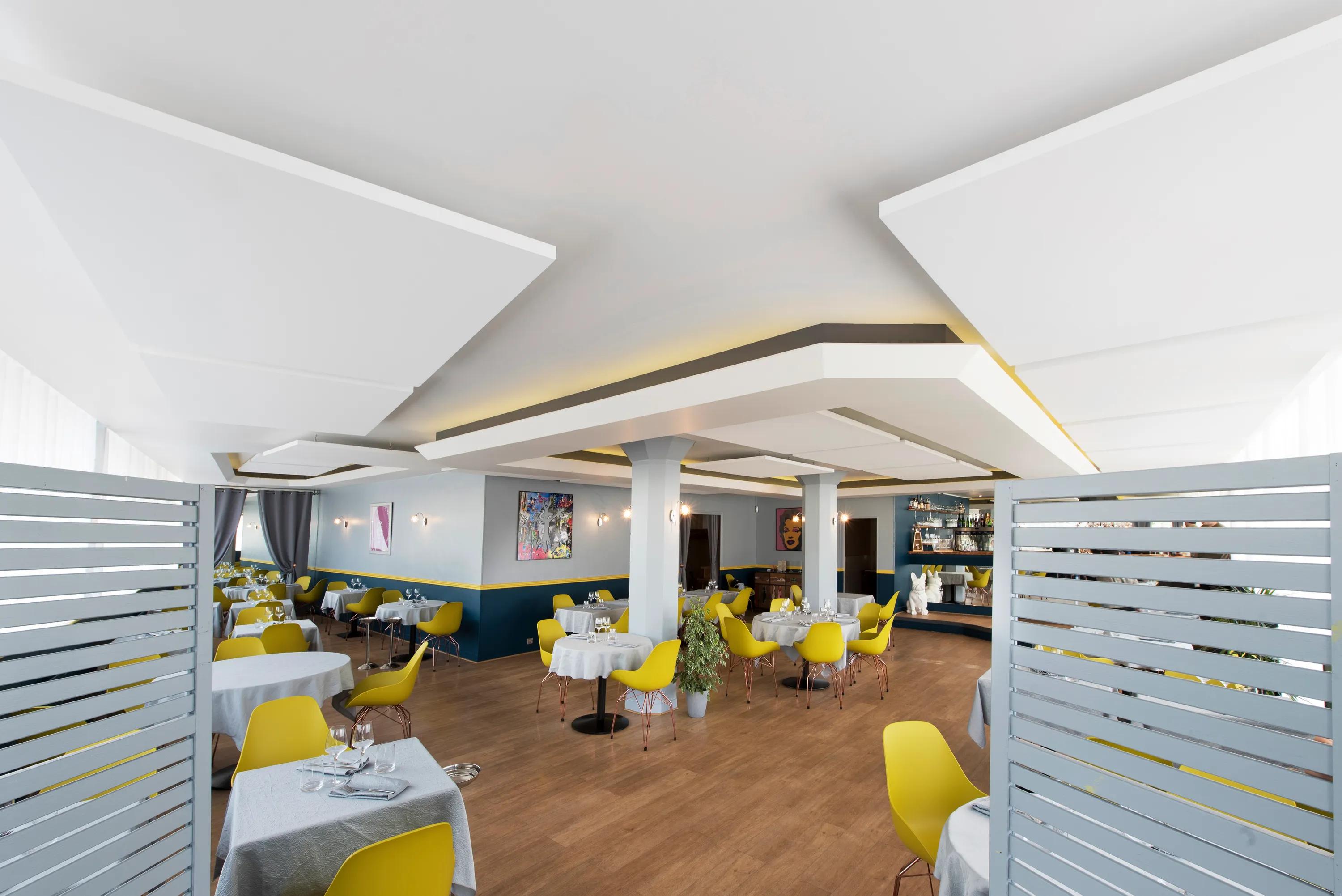Modern restaurant interior with yellow chairs, a floating raft ceiling, white tablecloths, wooden floor, contemporary decor, and soft lighting.