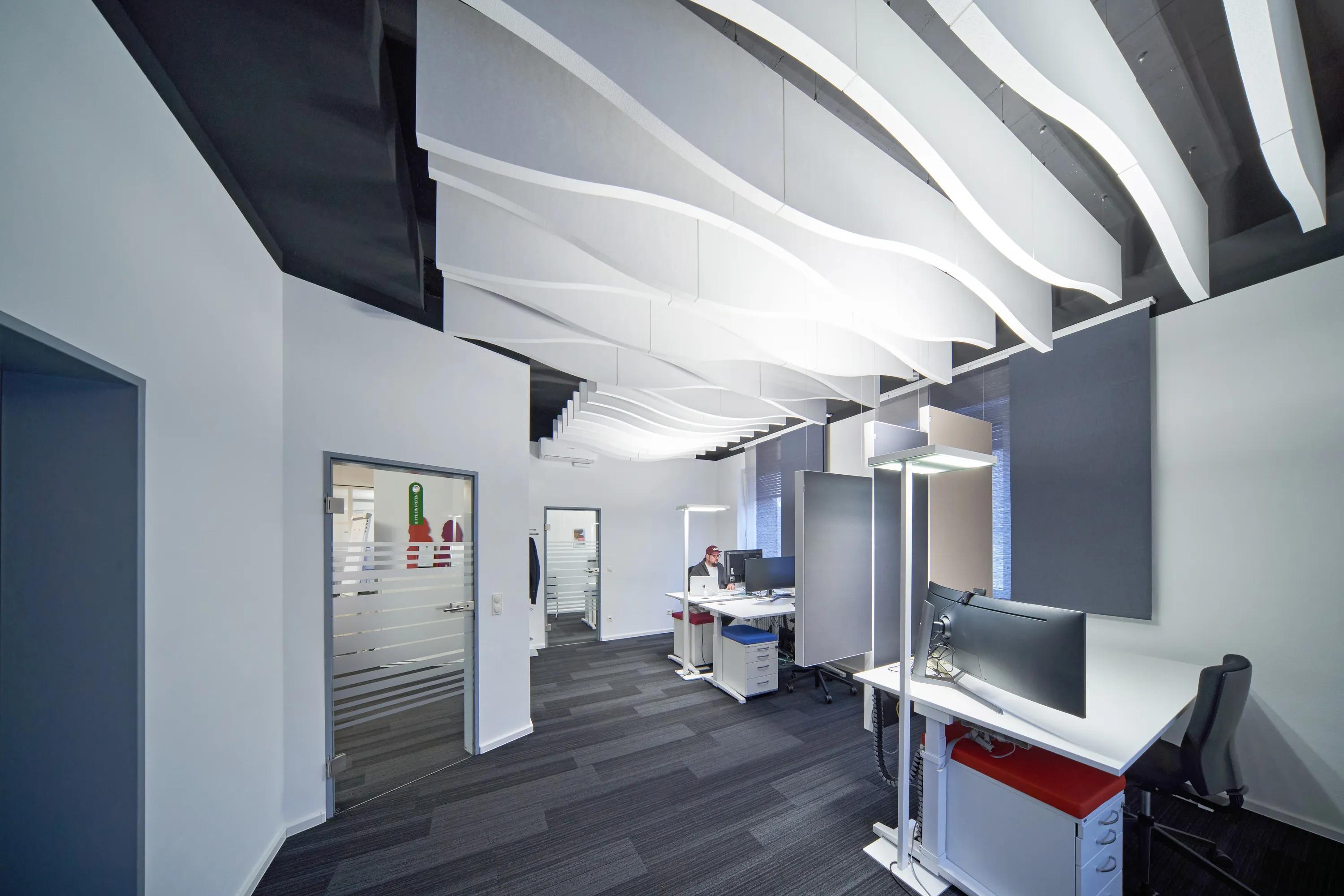 Office workspace with desks and white curved waved acoustic ceiling baffles suspended above the interior.