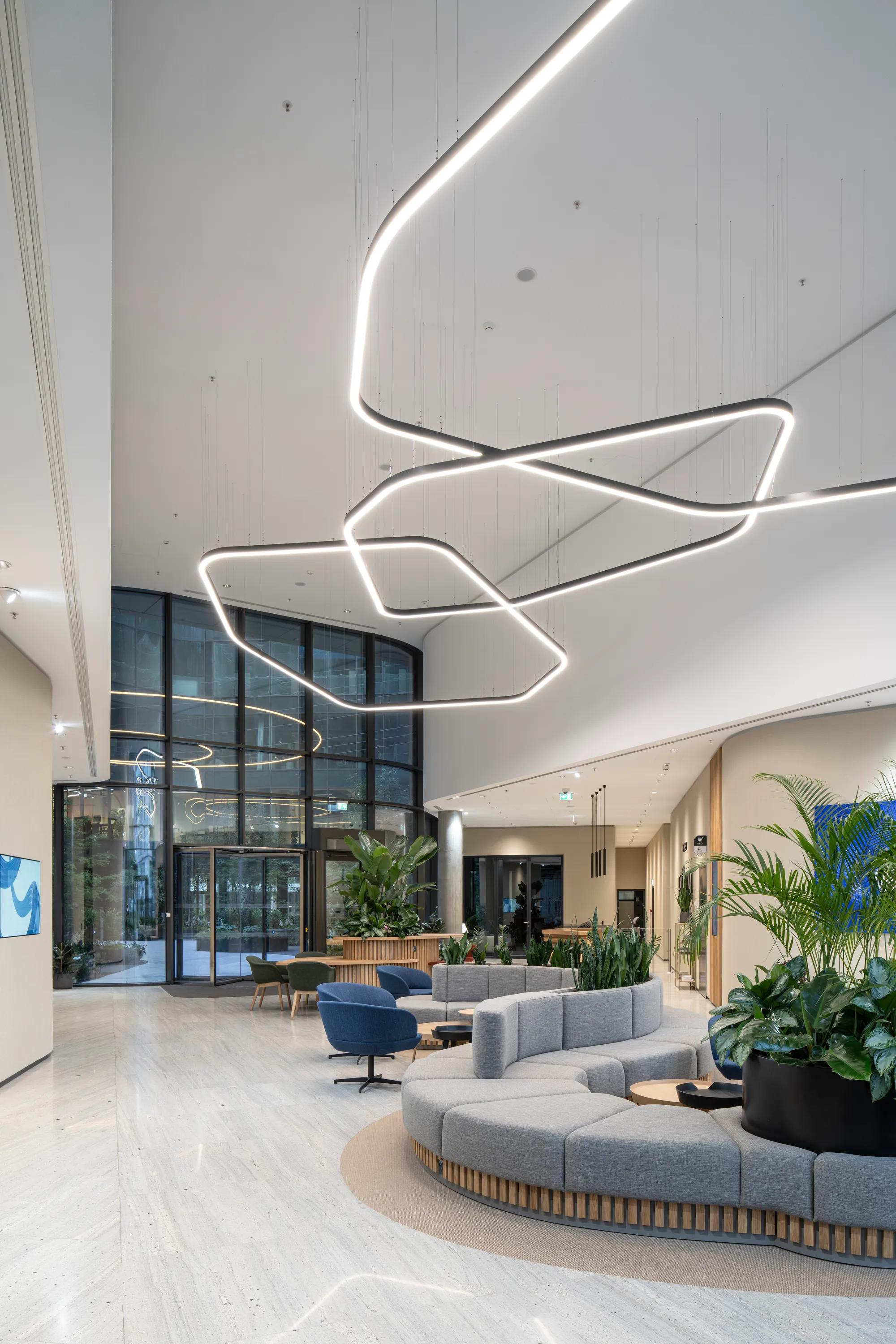 Elegant reception area with a smooth monolithic acoustic ceiling, suspended sculptural light installation, curved lounge seating, and abundant indoor planting