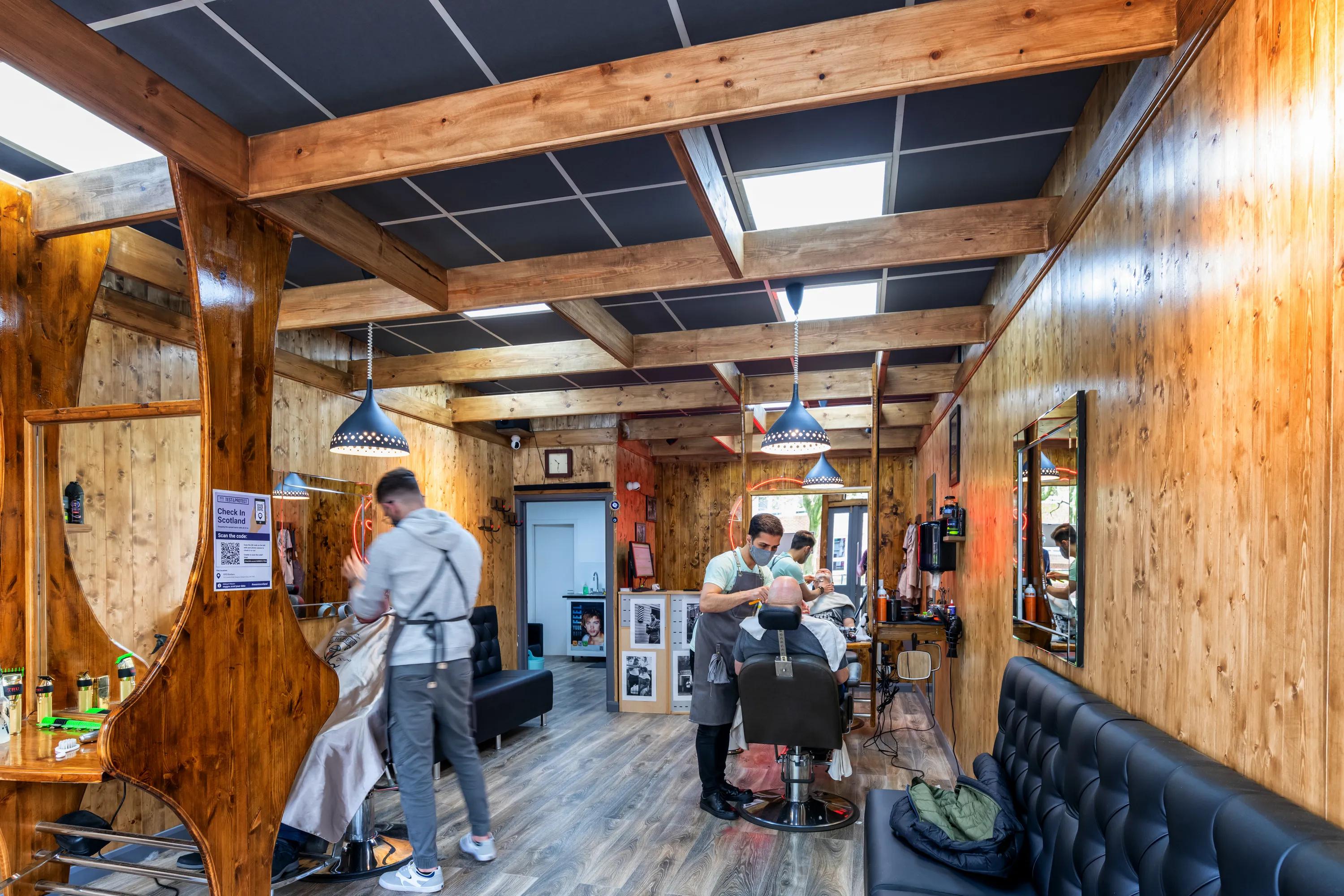 Barbershop interior with wooden walls, barber chairs, and black acoustic ceiling tiles installed between exposed timber beams.