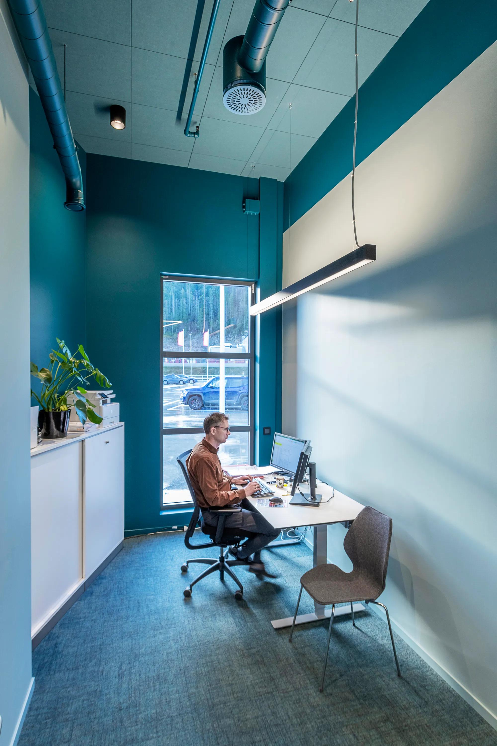 Man working at a desk in a small office with coloured acoustic ceiling panels and exposed ventilation ducts