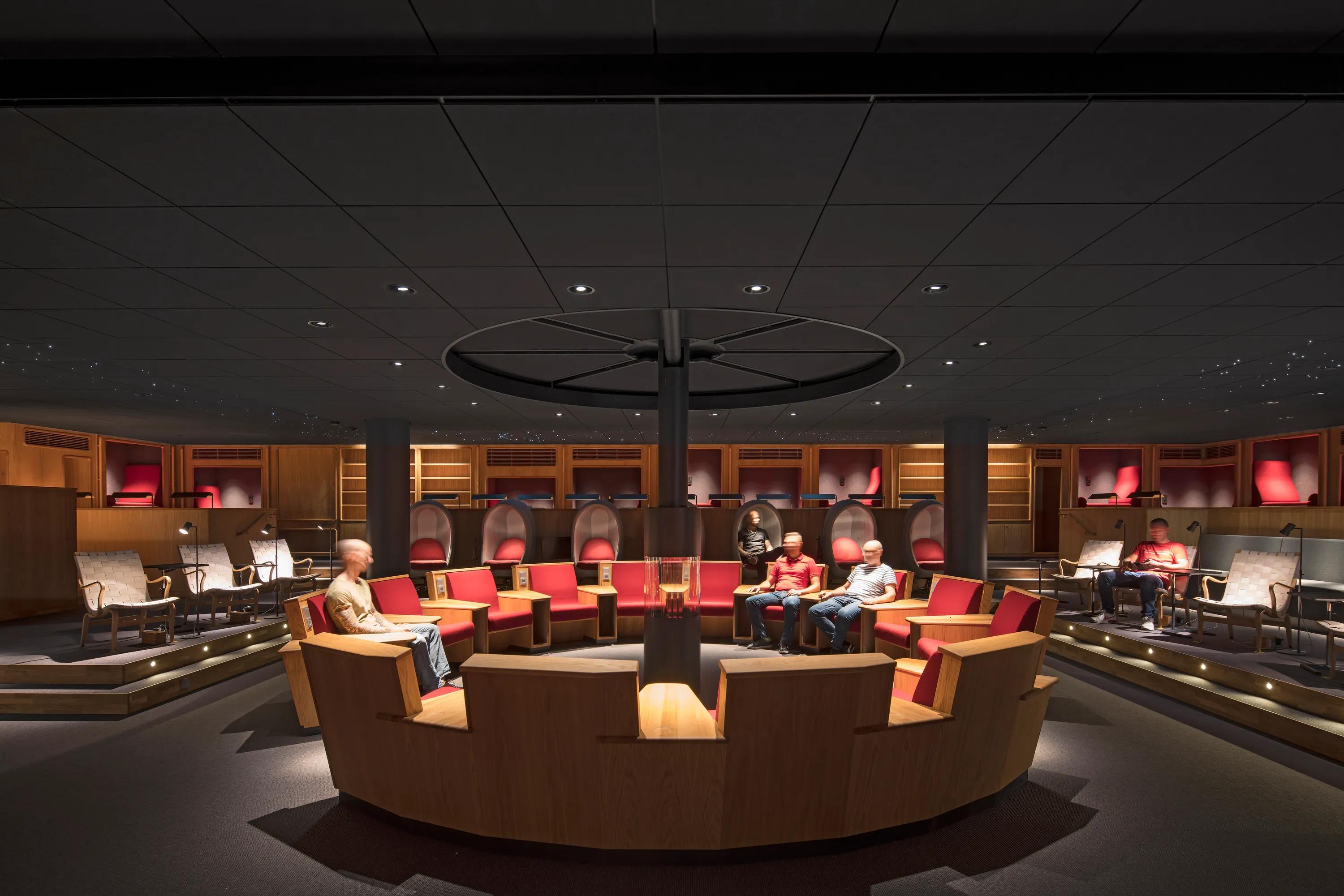 A modern conference room with black suspended ceiling and starry lighting, circular seating, red accents, and dim lighting. People are seated around the room.