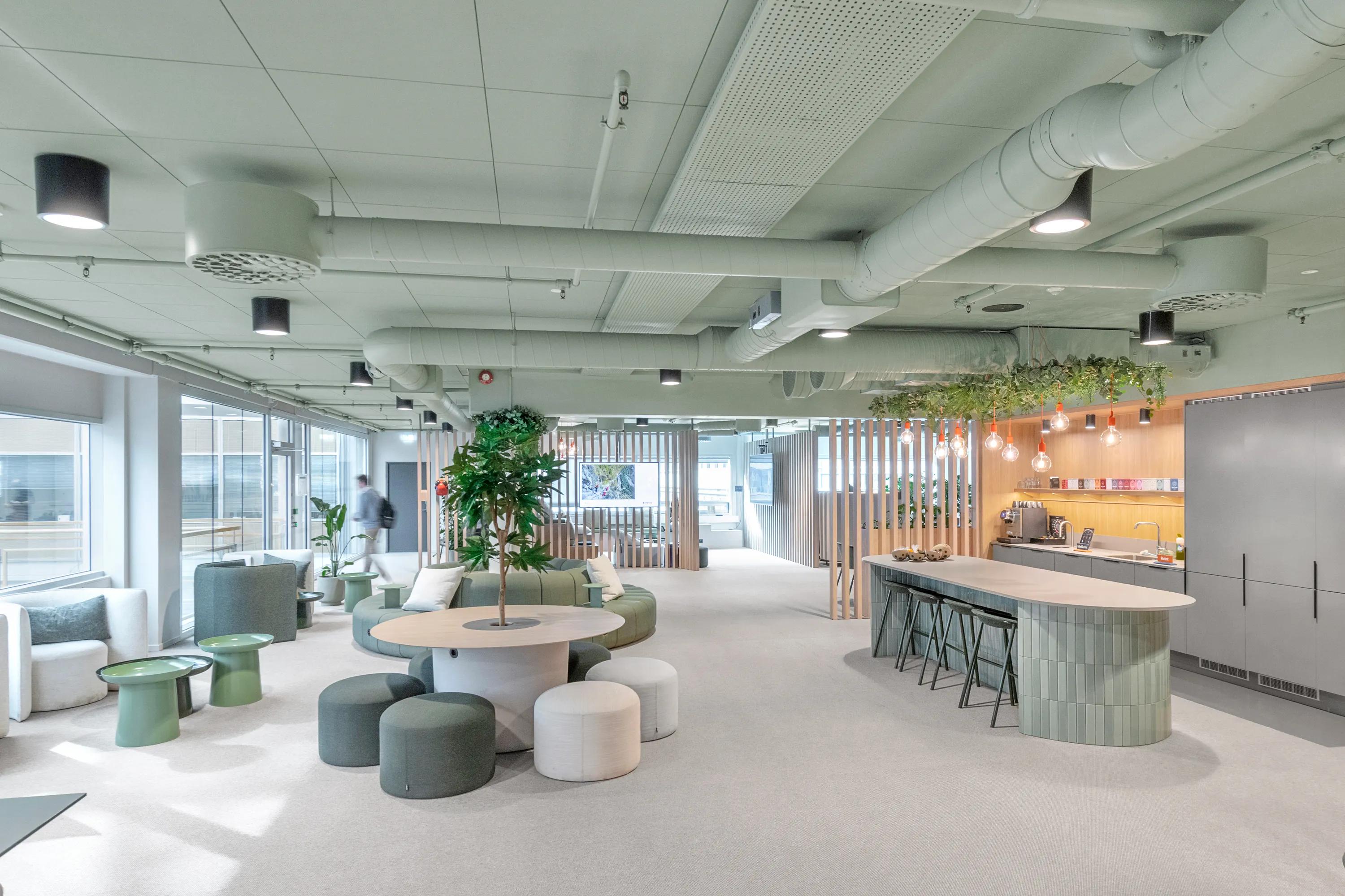 Modern green office ceiling with pastel green decor, round tables, cushioned stools, a long counter with bar stools, and large windows.