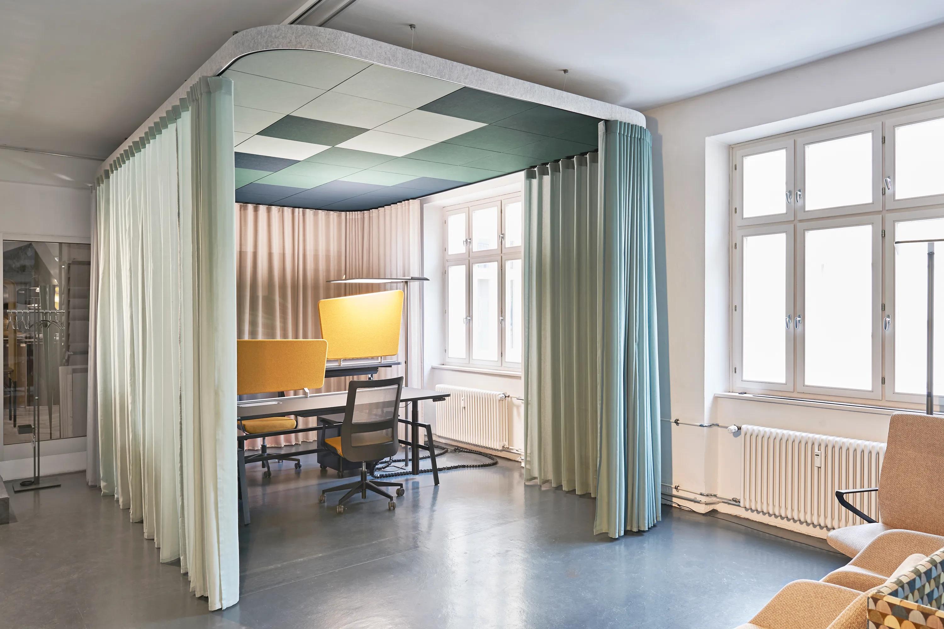 Modern office nook with green ceiling design, a table, chairs, and translucent curtains in a bright room with large windows.