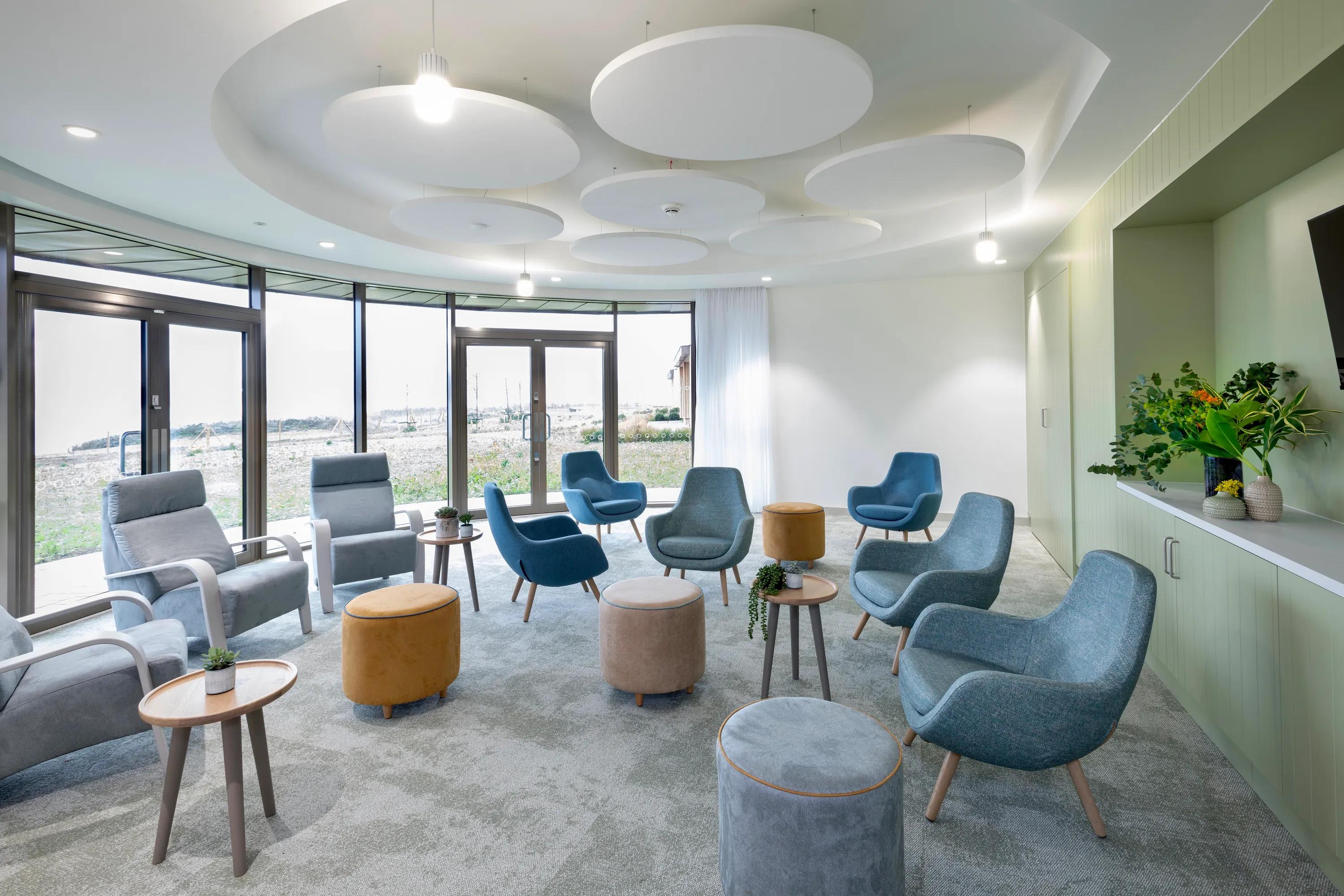 A calm, light-filled lounge with soft seating arranged in a circle and large white circular acoustic rafts suspended from the ceiling.