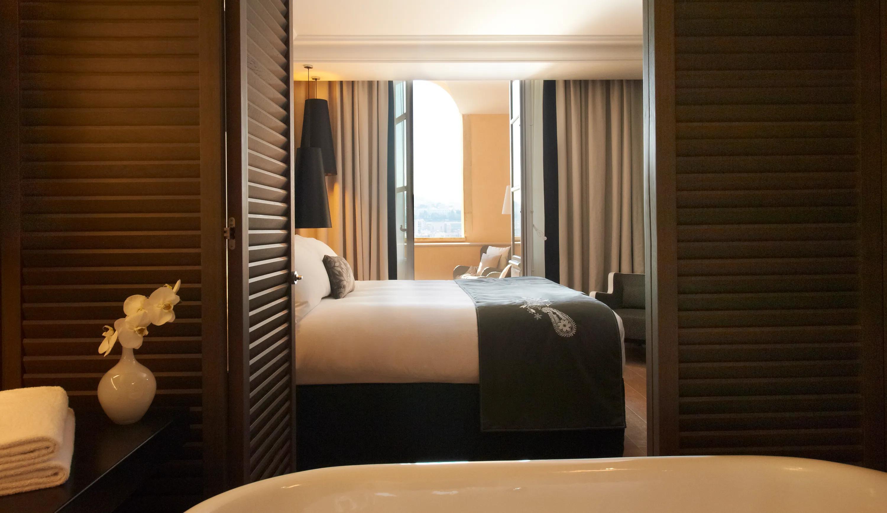Hotel bedroom interior with a large bed, pendant lighting, and a smooth white acoustic ceiling above the room.