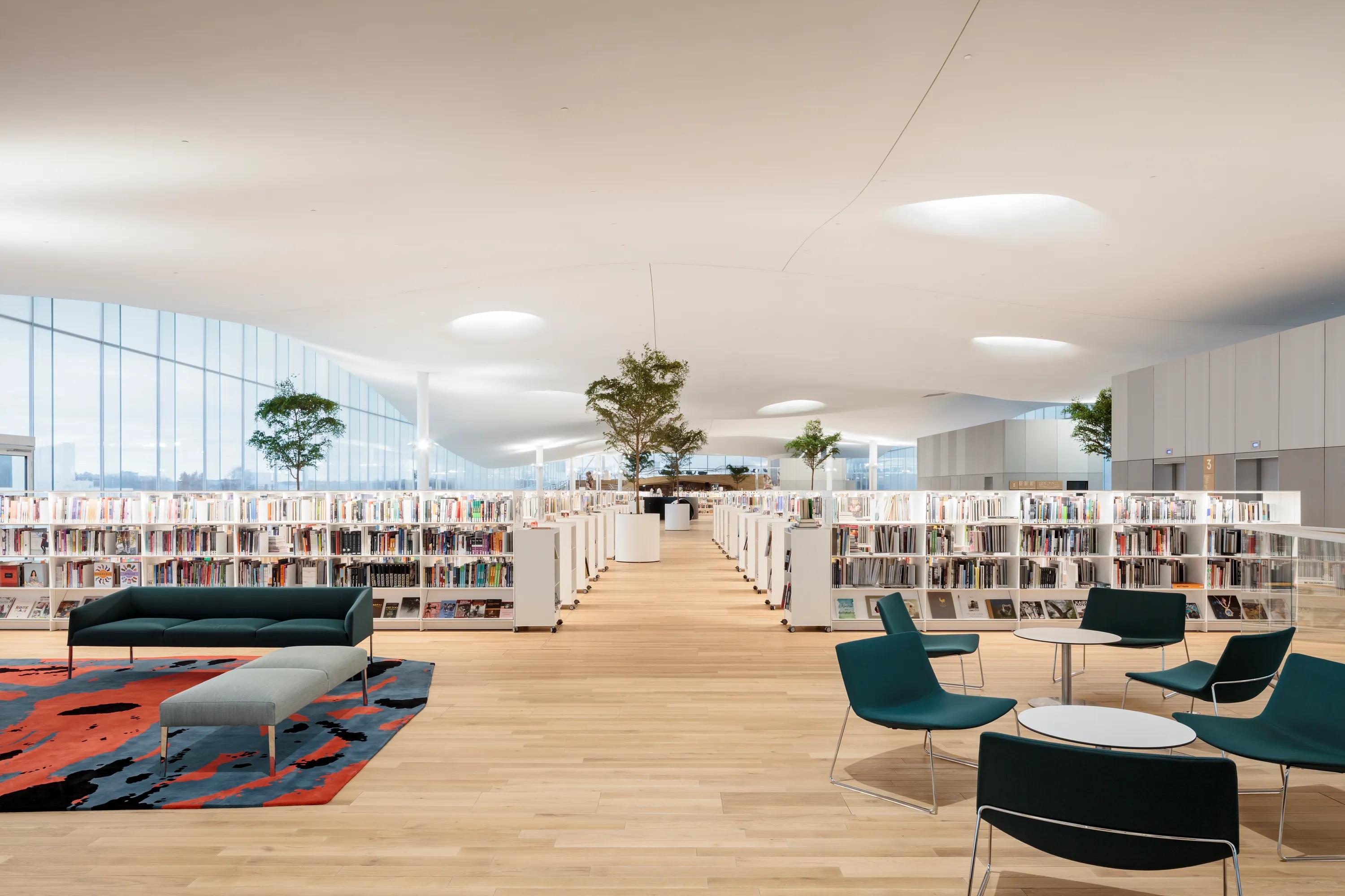 A bright open-plan library interior with a seamless white Rockfon Mono Acoustic ceiling above long rows of bookshelves and reading areas at Oodi Library