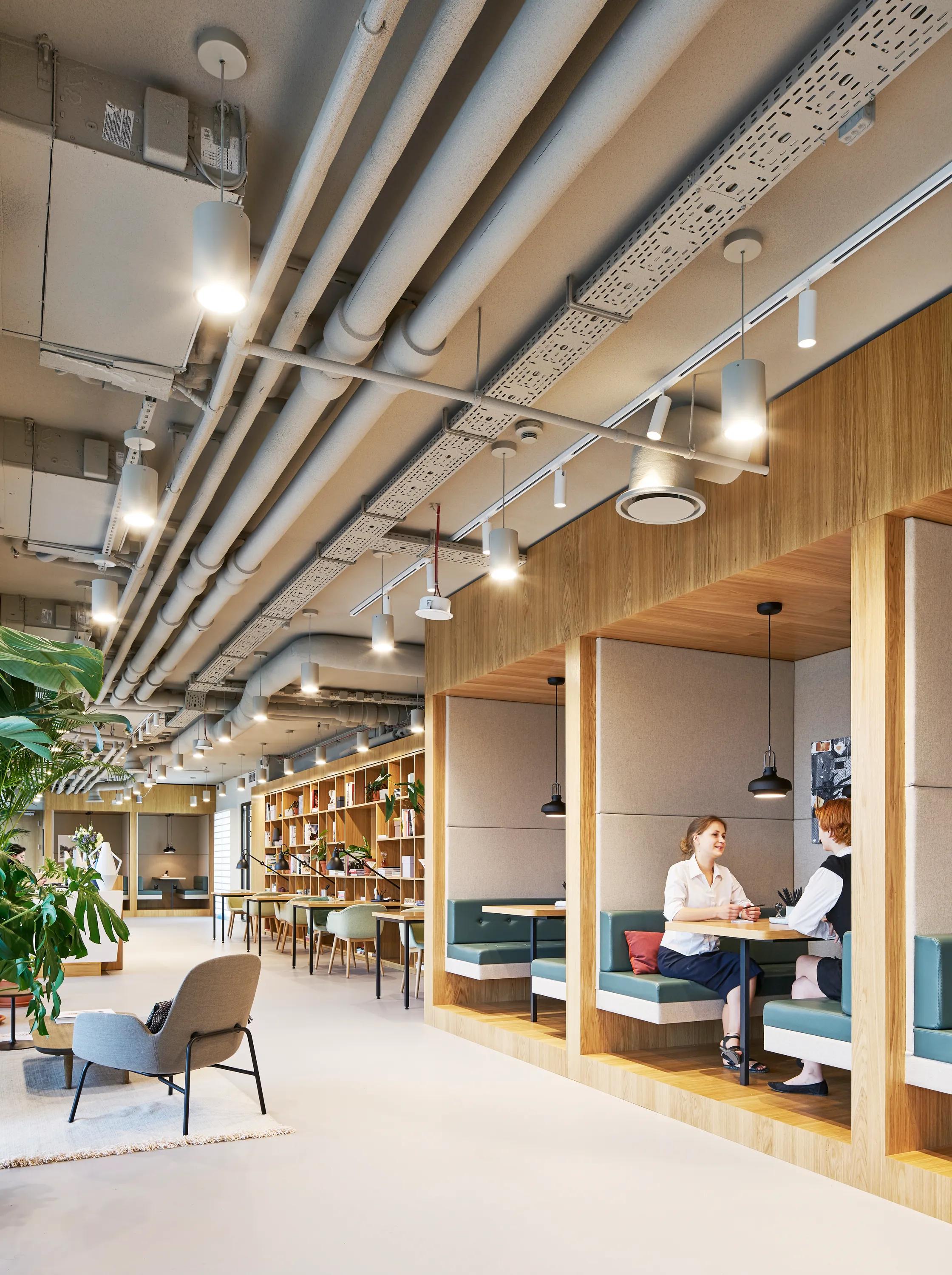 Workspace interior with a coloured monolithic acoustic ceiling and exposed mechanical services above wooden booth seating