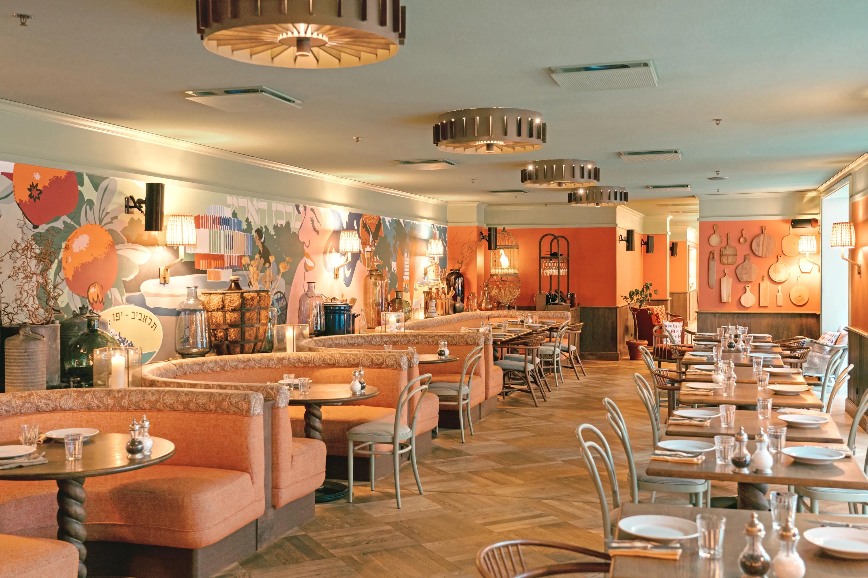 Stylish restaurant interior with orange walls, patterned booths, wooden tables, chairs, decorative wall art, and ambient lighting.