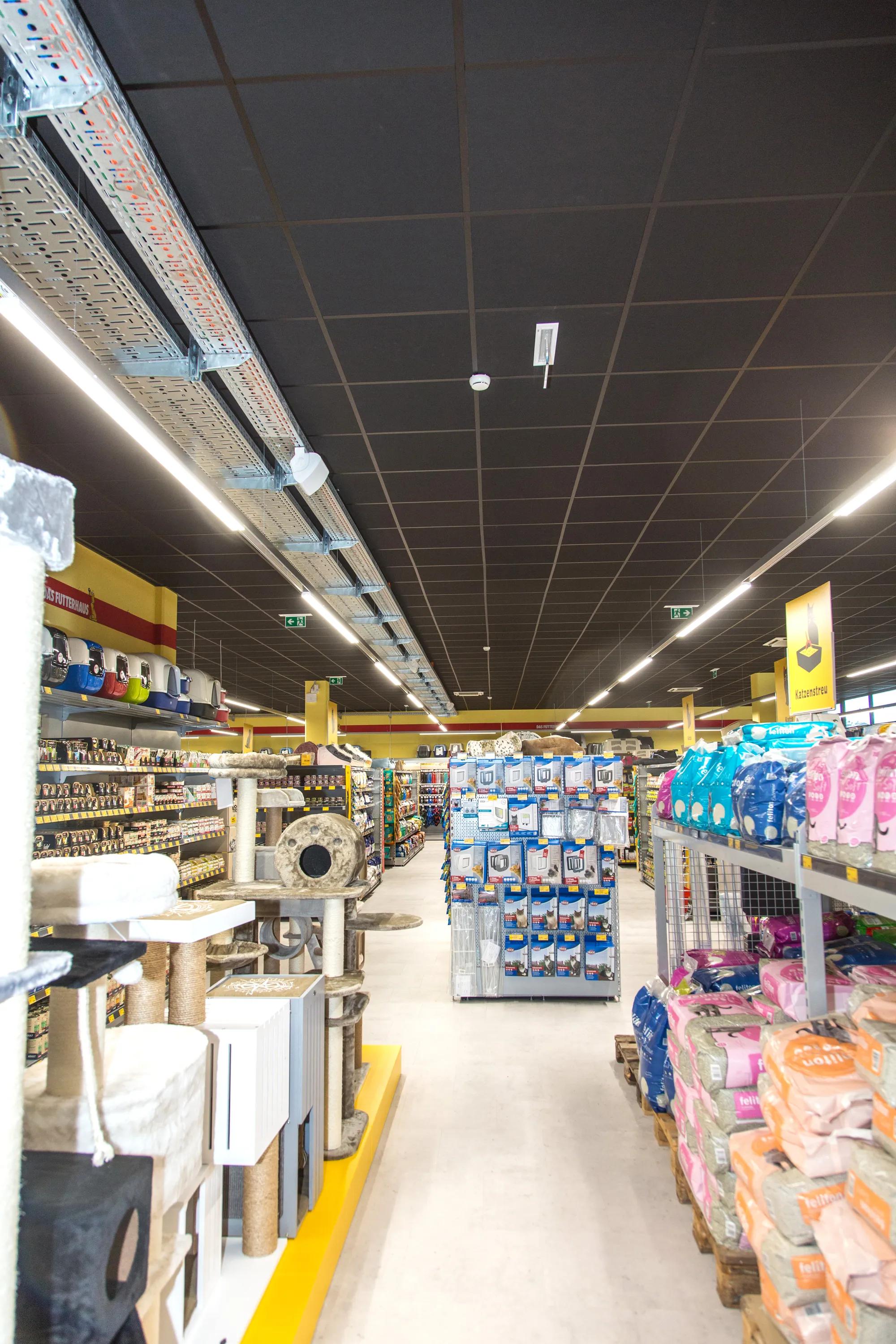 Pet supply store aisle with shelves of products and a black acoustic grid ceiling with integrated linear lighting above the retail space.