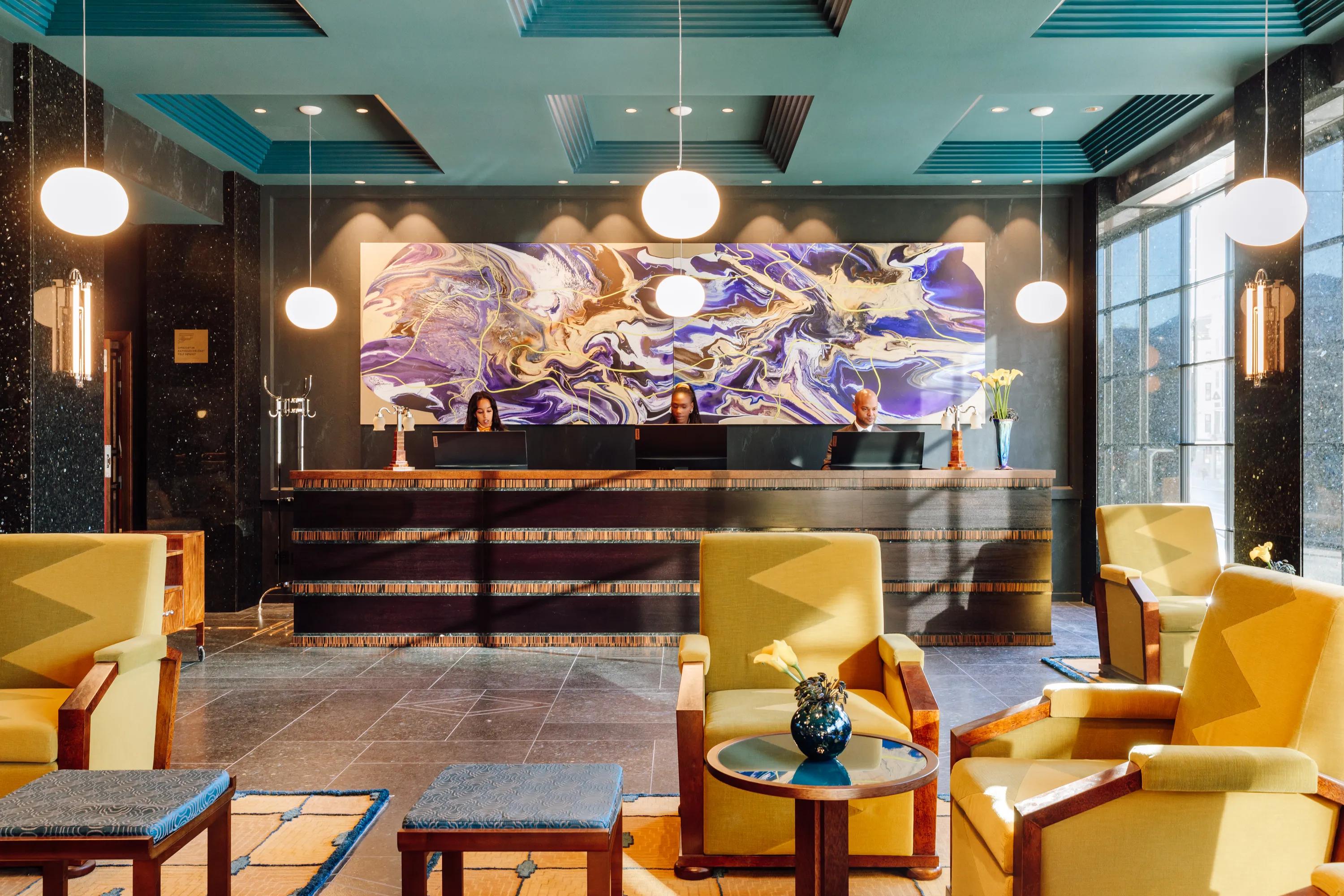 Hotel reception lobby with seating area, front desk, and coloured acoustic ceiling panels with recessed lighting above the space.