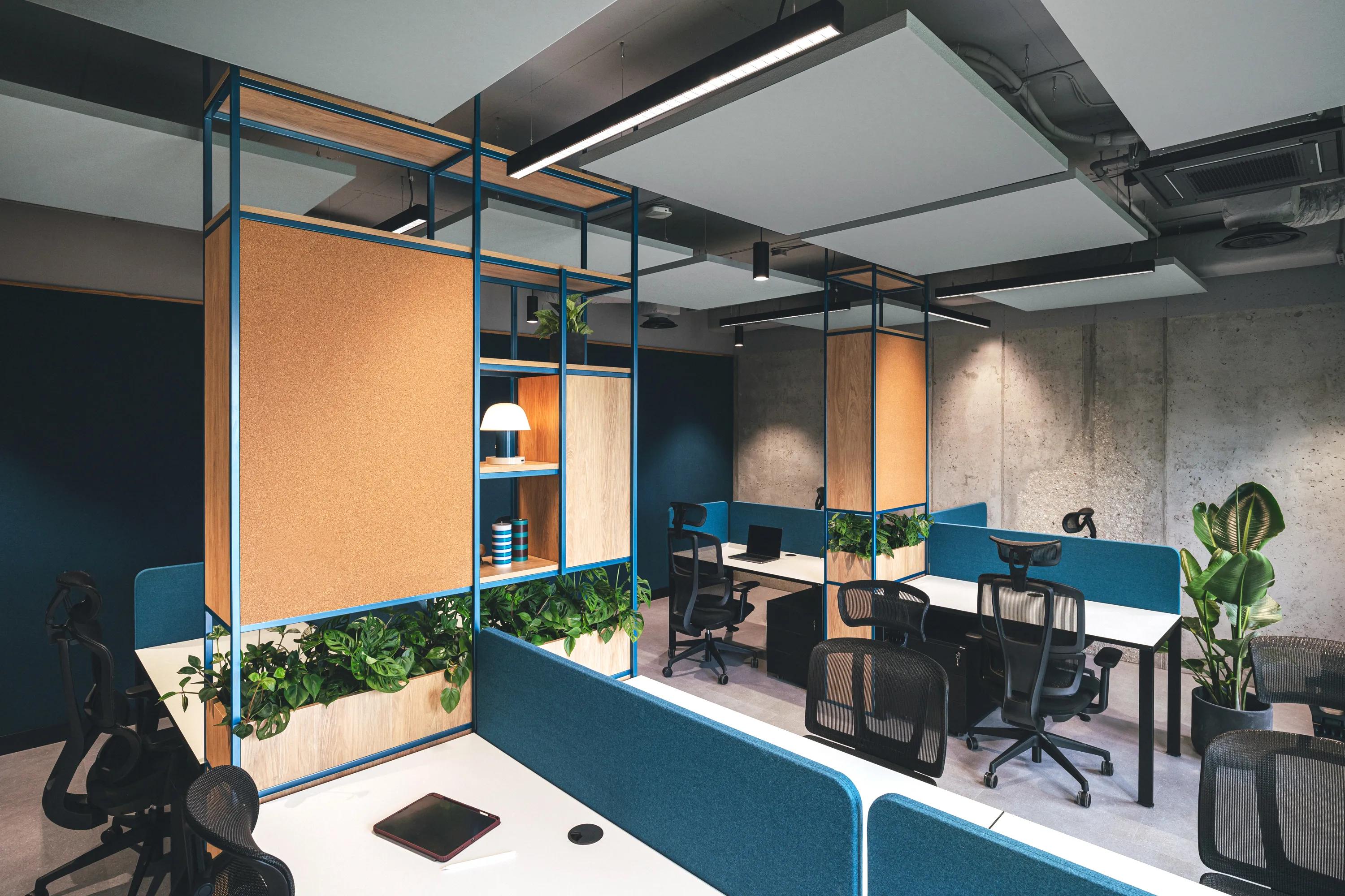 Modern office space with floating panels in the office ceiling, multiple workstations, blue partitions, plants, shelves, and overhead lighting in a stylish, open layout.