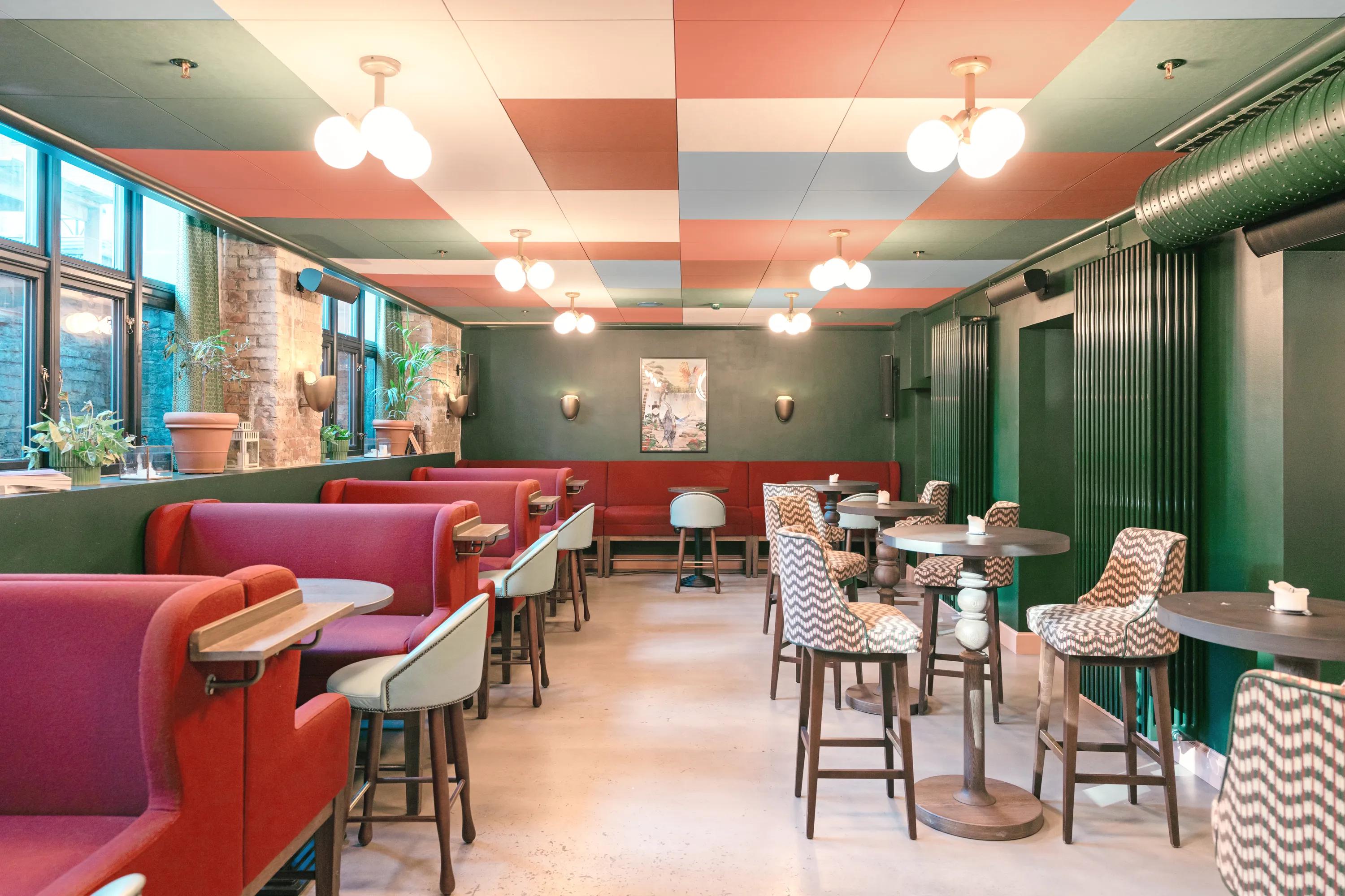 Café interior with a colourful checkerboard acoustic ceiling, red booth seating, green walls, and high tables arranged along the dining area.