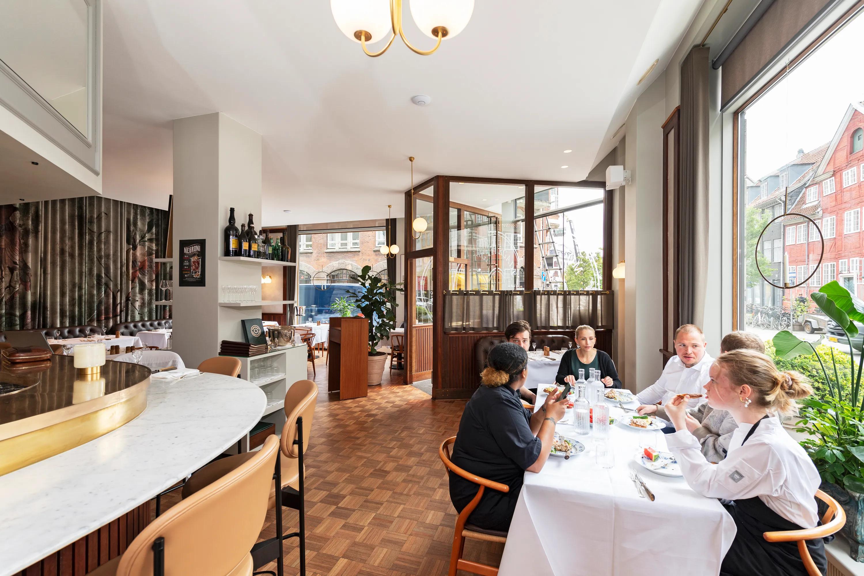 A group of people dining together without the Lombard Effect at a bright, modern restaurant with large windows and stylish decor.