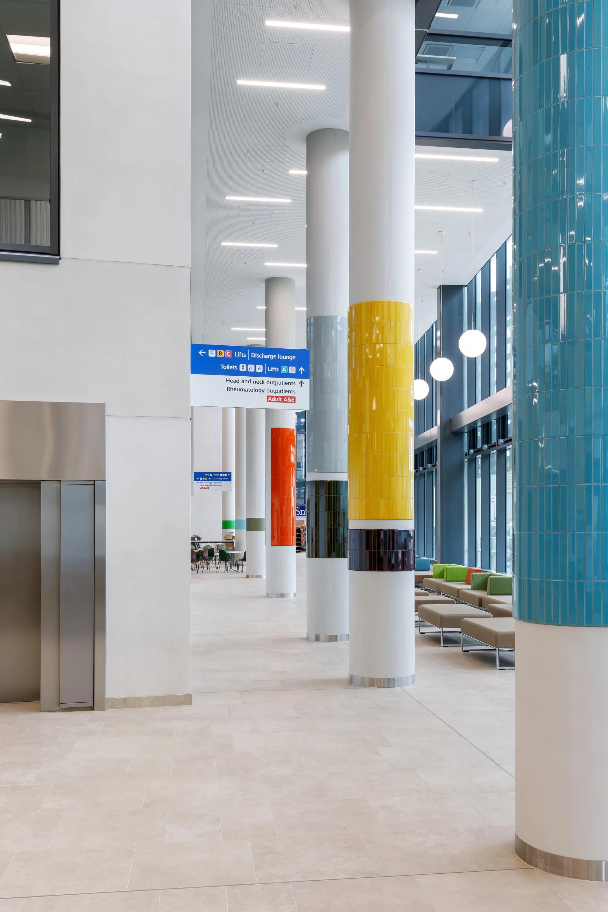 Multicoloured tiled pillars and modern seating in a bright hospital lobby with high ceilings and large windows.