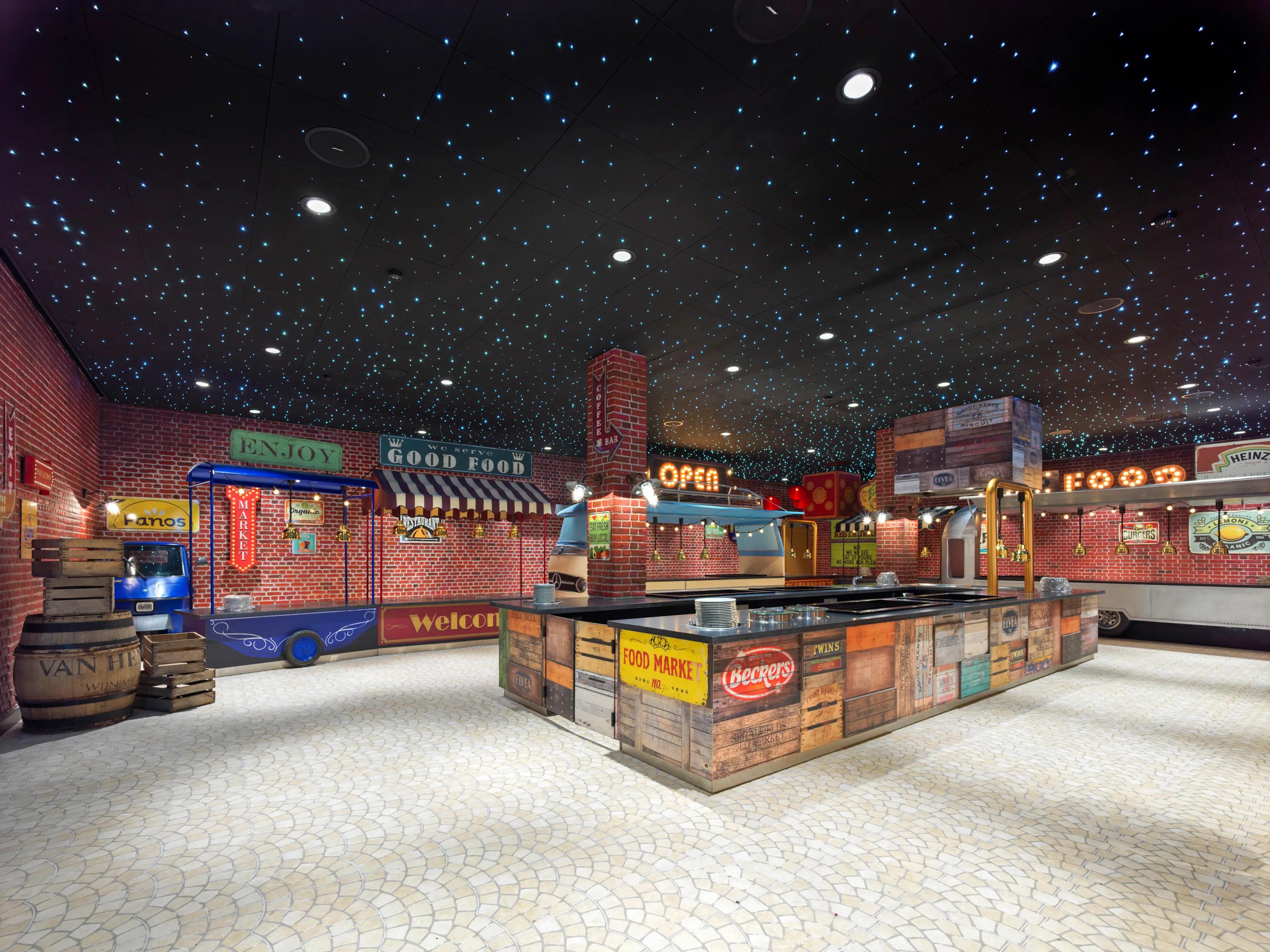 A colorful indoor market scene with black suspended ceiling and starry lighting, brick walls, vintage signs, and a starry ceiling, featuring a central counter and various food stalls.