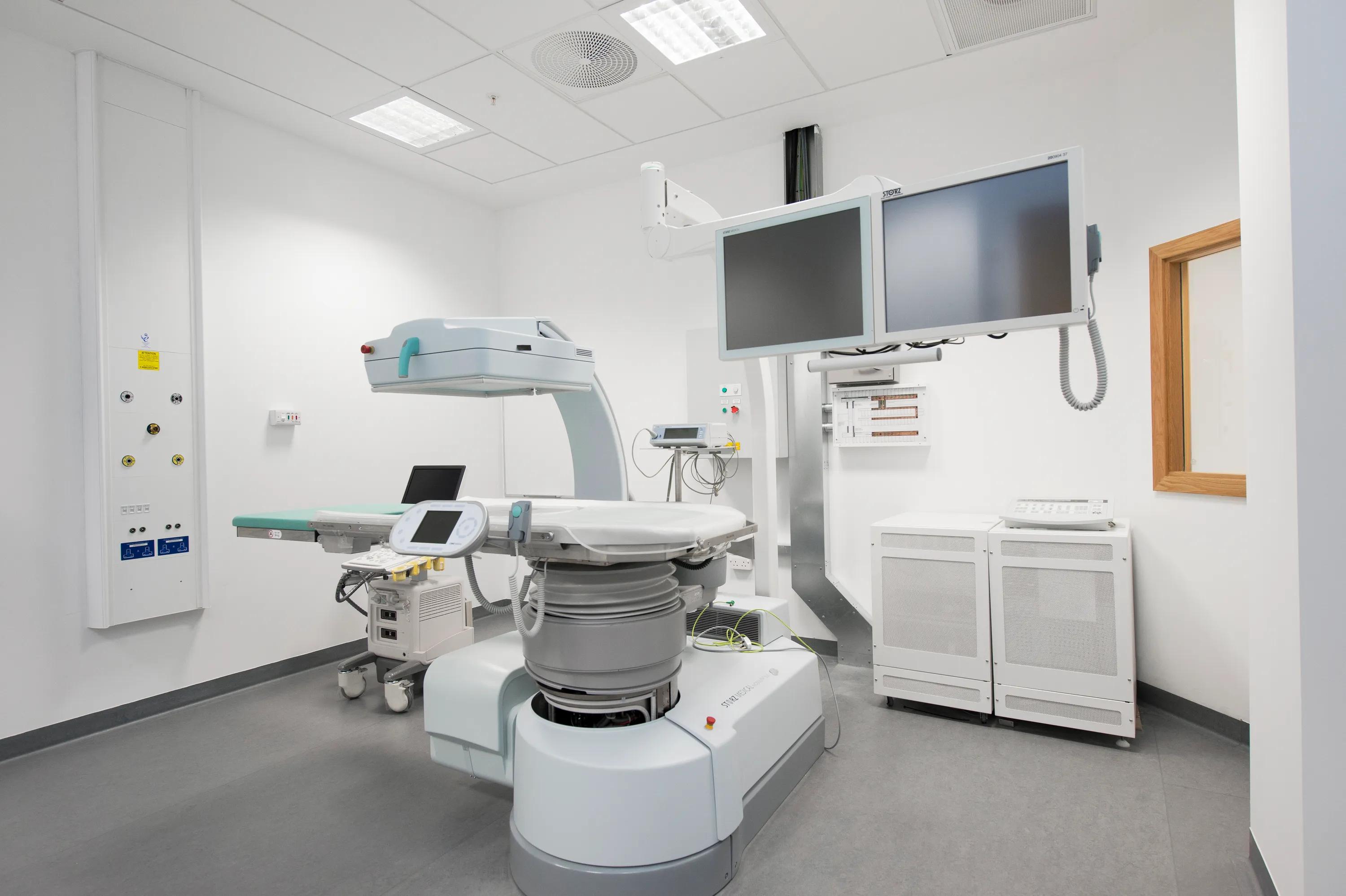 A clinical imaging suite containing advanced diagnostic equipment beneath a hygienic acoustic ceiling with integrated ventilation and lighting units.