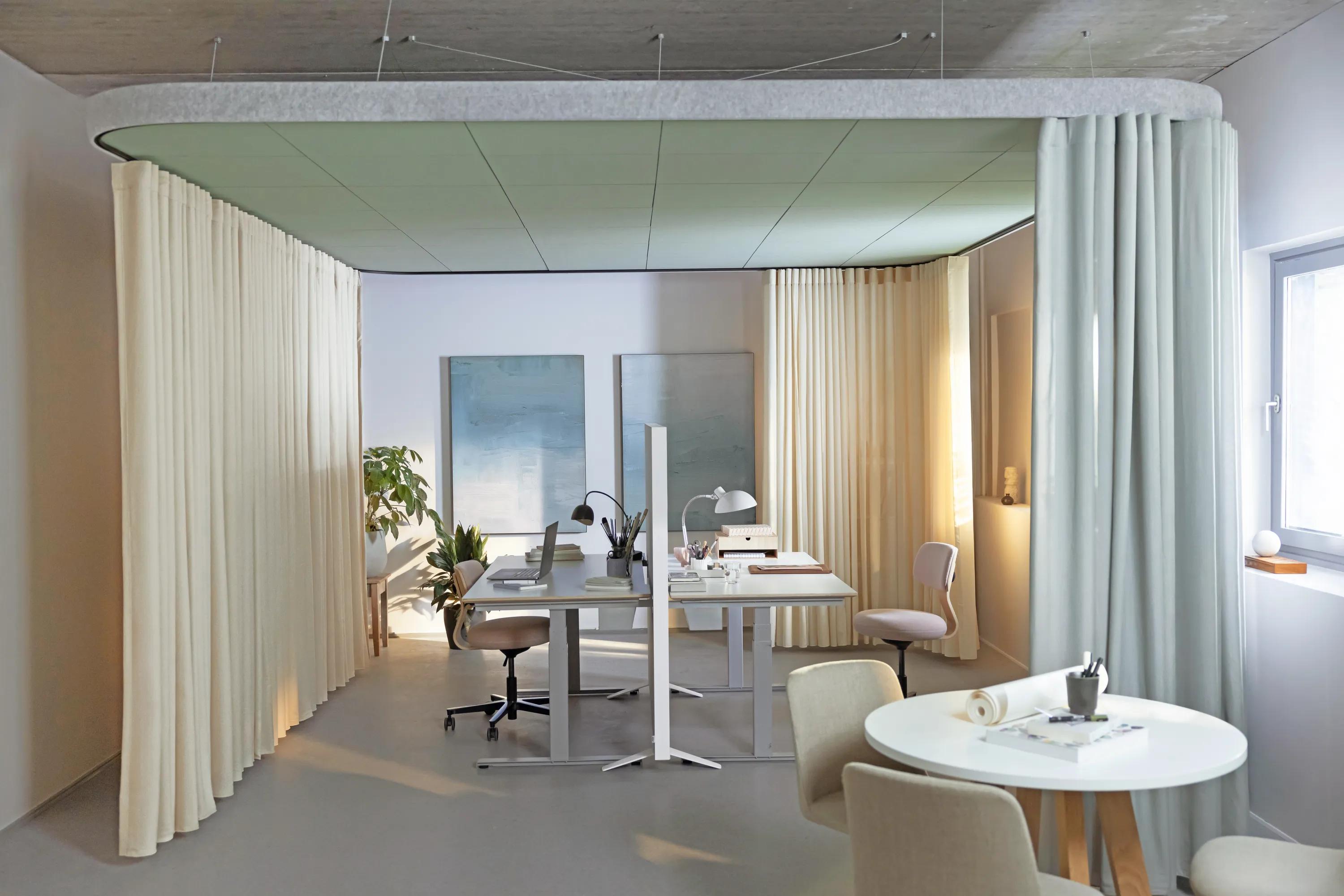 Workspace with suspended coloured acoustic ceiling panels forming a canopy above two desks, surrounded by floor-to-ceiling curtains