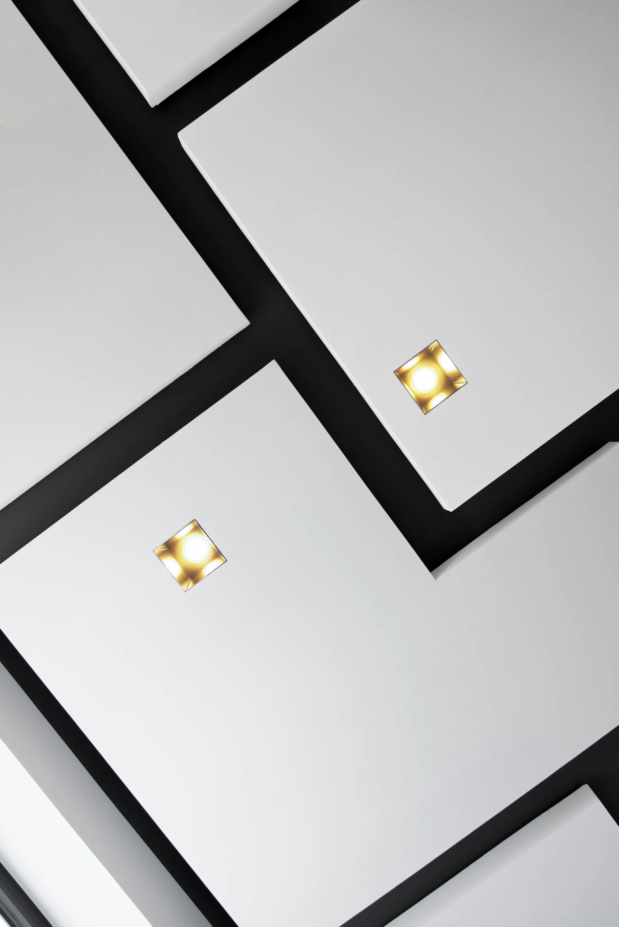 Close-up view of white acoustic ceiling panels installed against a dark background, with integrated square recessed lights