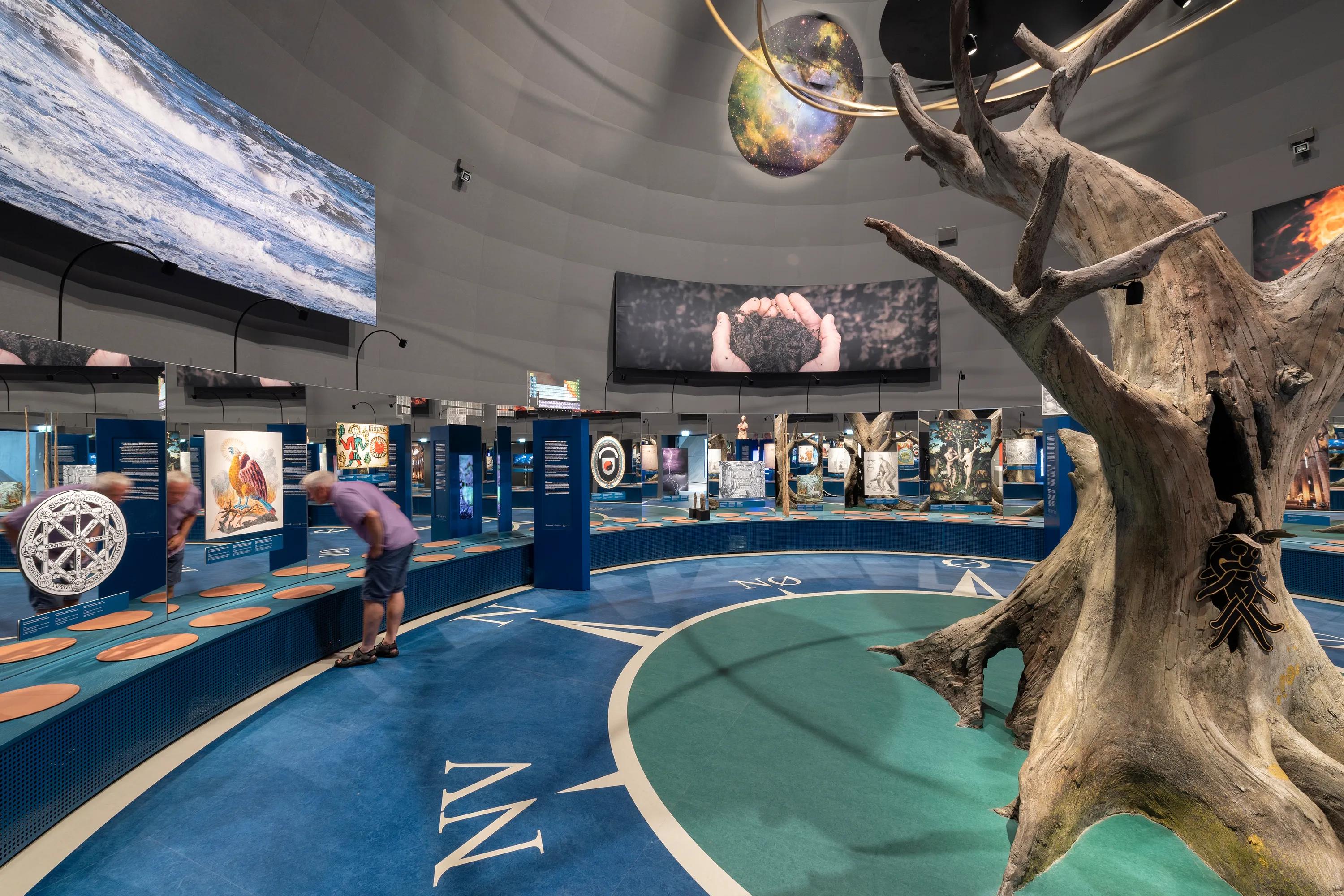 Naturkraft exhibition space featuring a dome-shaped Rockfon Color-all acoustic ceiling installation, with a central tree sculpture, suspended planet models, and interactive displays arranged around the circular gallery.