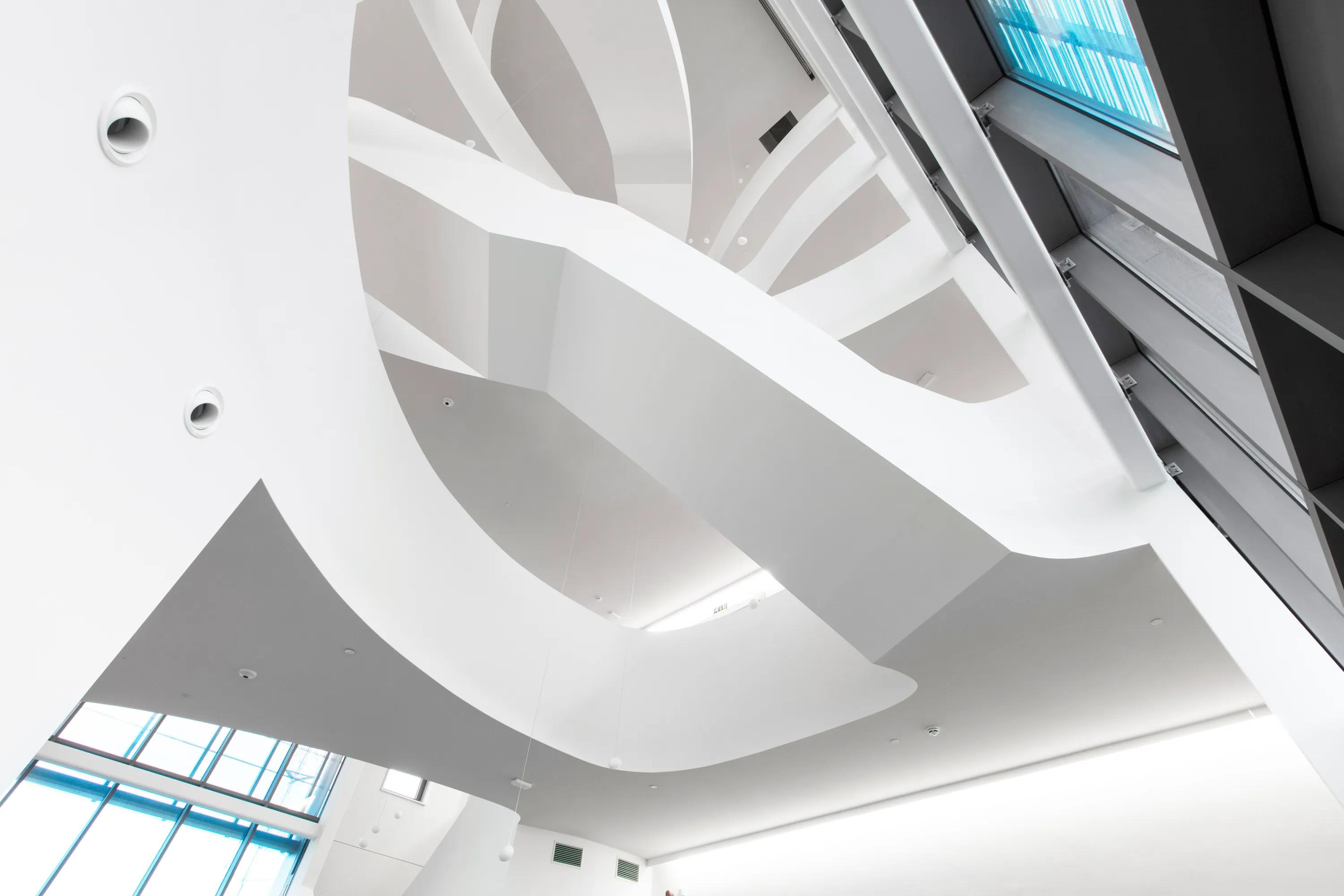 Contemporary multi-storey atrium showcasing a monolithic acoustic ceiling with sculptural white curves, integrated lighting, and tall skylights illuminating the lobby