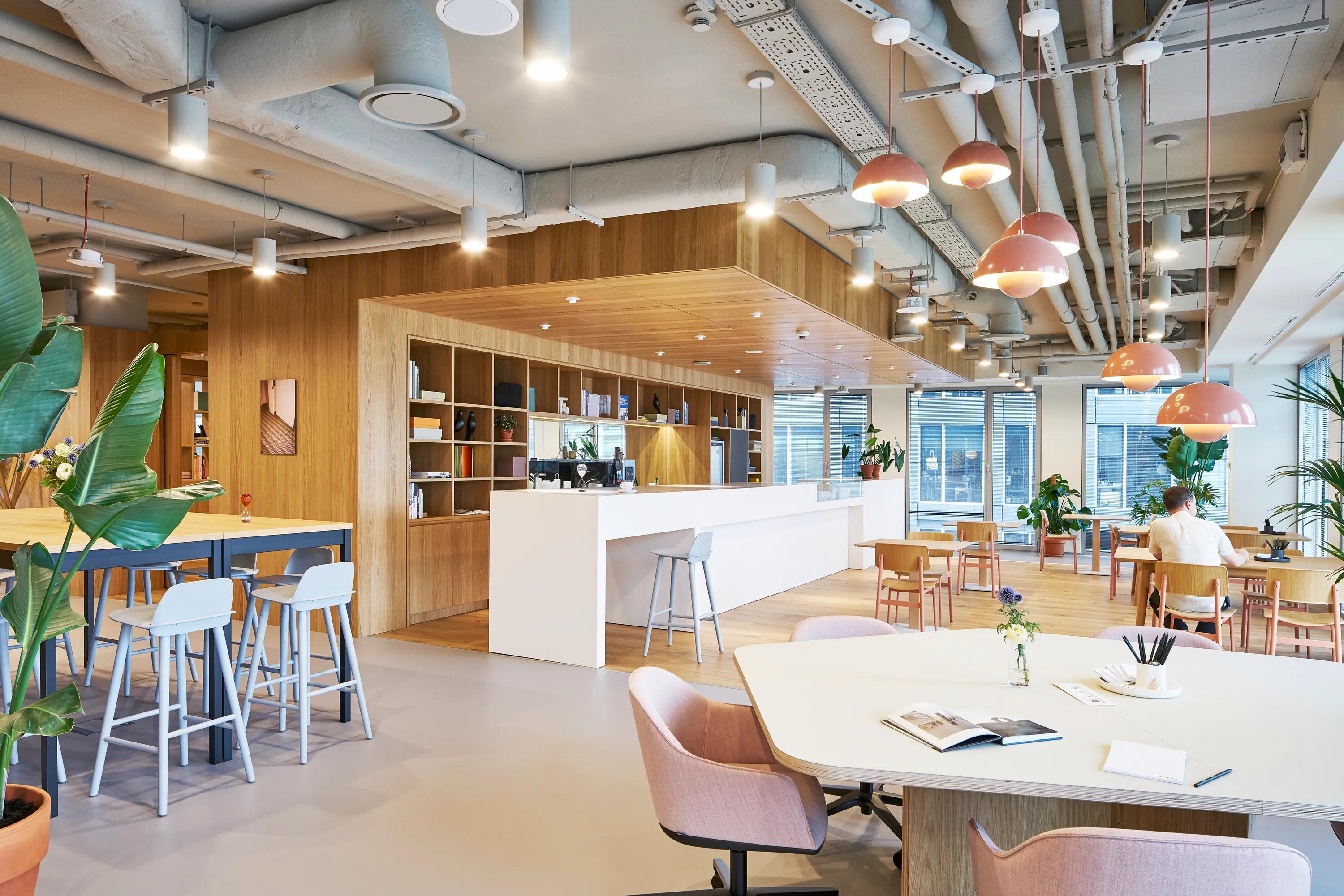 Flexible workspace with a seamless coloured monolithic acoustic ceiling above exposed services, complemented by warm timber finishes and mixed seating zones