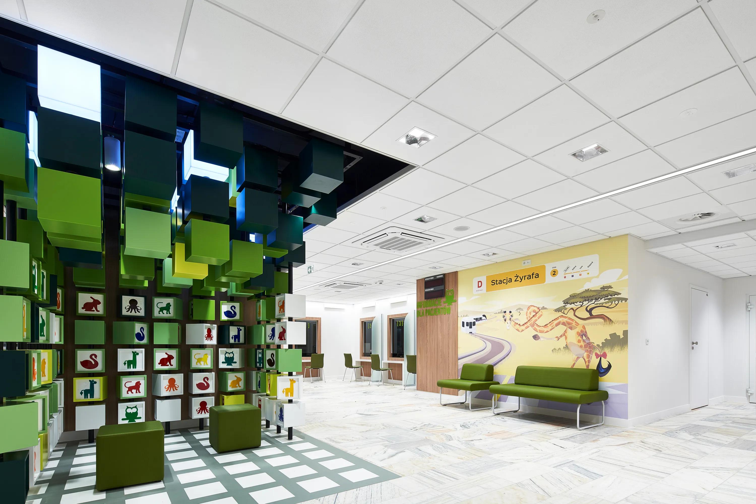 A bright paediatric waiting area featuring a suspended installation of colourful green cubes, playful animal graphics on wall panels, and a clean white acoustic ceiling with integrated lighting.