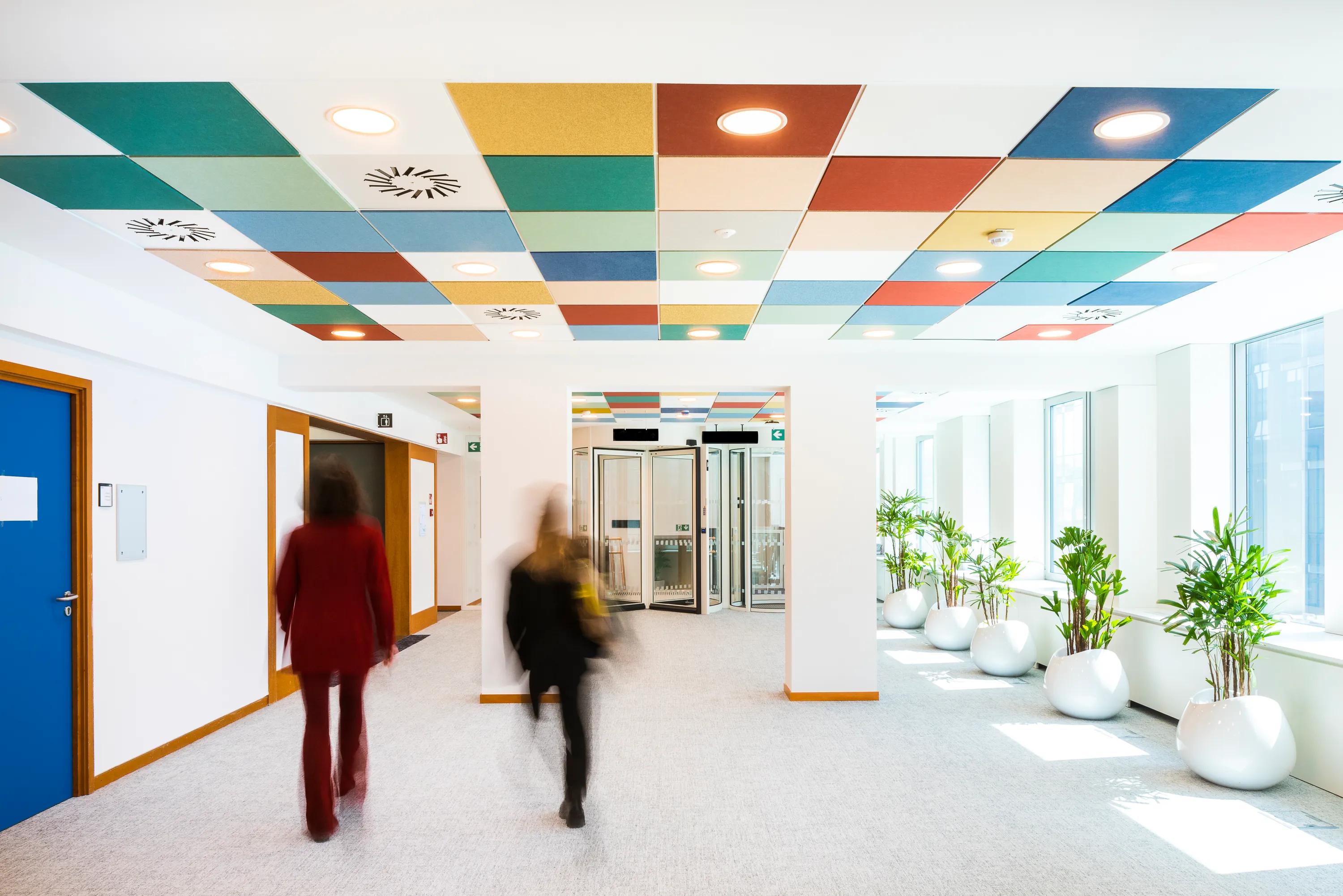 Office corridor with colourful checked acoustic ceiling tiles arranged in a geometric pattern above the walkway.