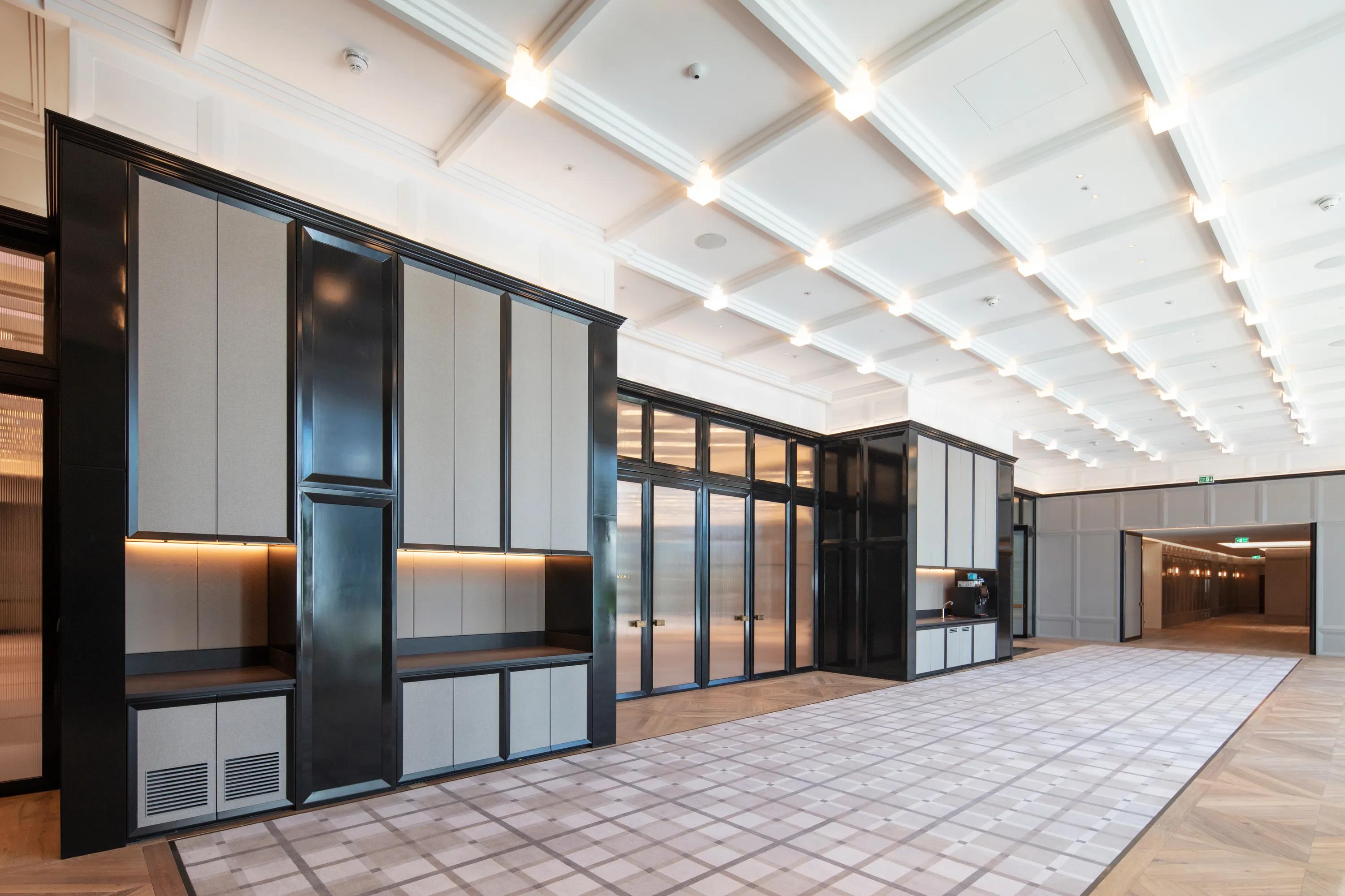 Luxury hotel lobby with reception desk, large artwork, sculptural lighting installation, and a white coffered acoustic ceiling above the space.