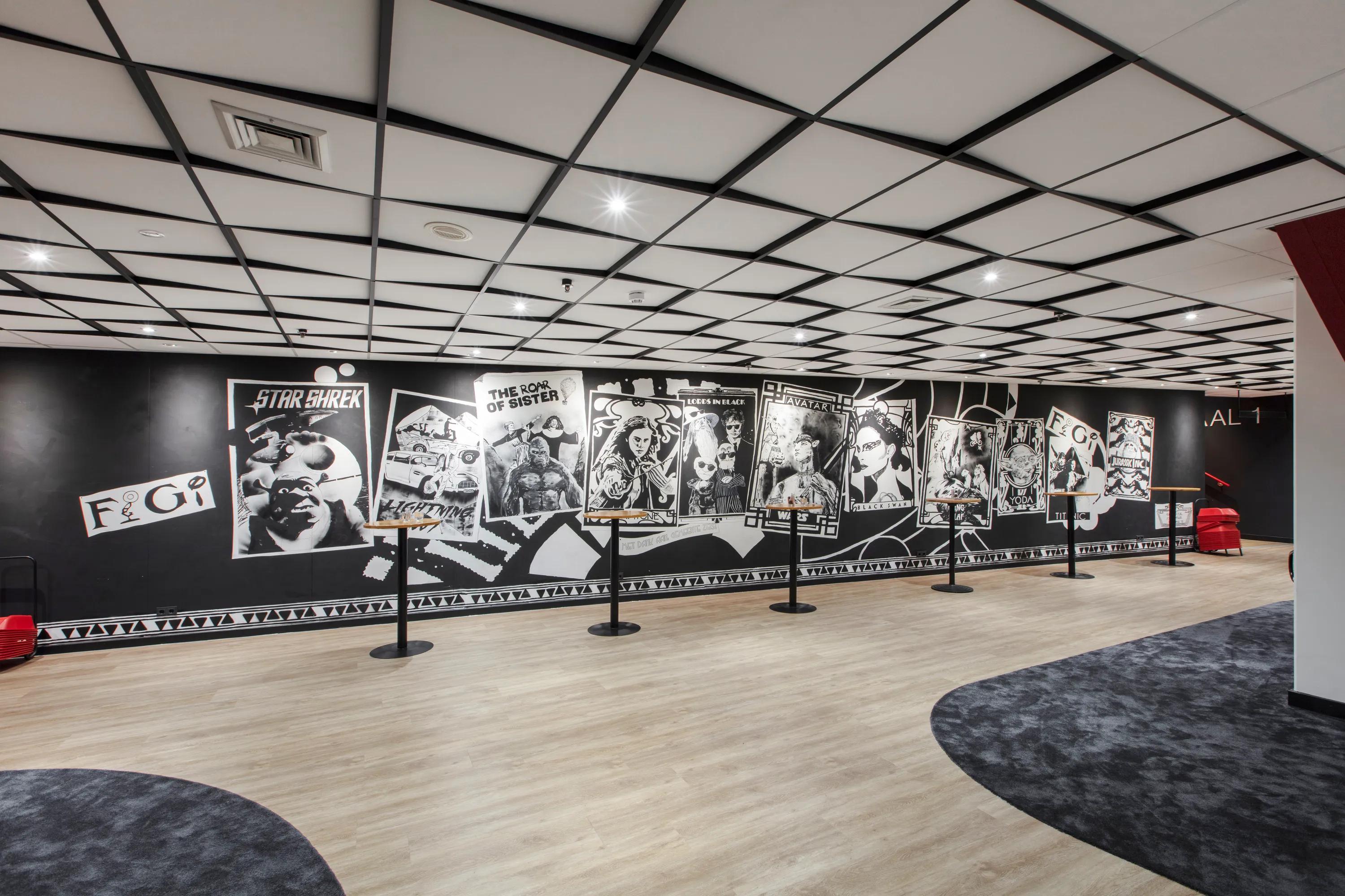 Hotel Theater Figi waiting area with graphic mural walls and a grid acoustic ceiling above the open foyer space.